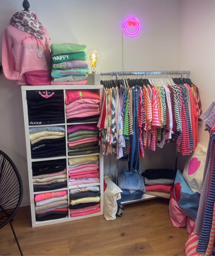 Regal mit gefalteten Shirts und Kleiderstange voller bunter Oberteile in der Boutique